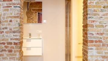 Un couloir étroit avec un mur en briques, un plafond en bois et une cabine de douche en verre.