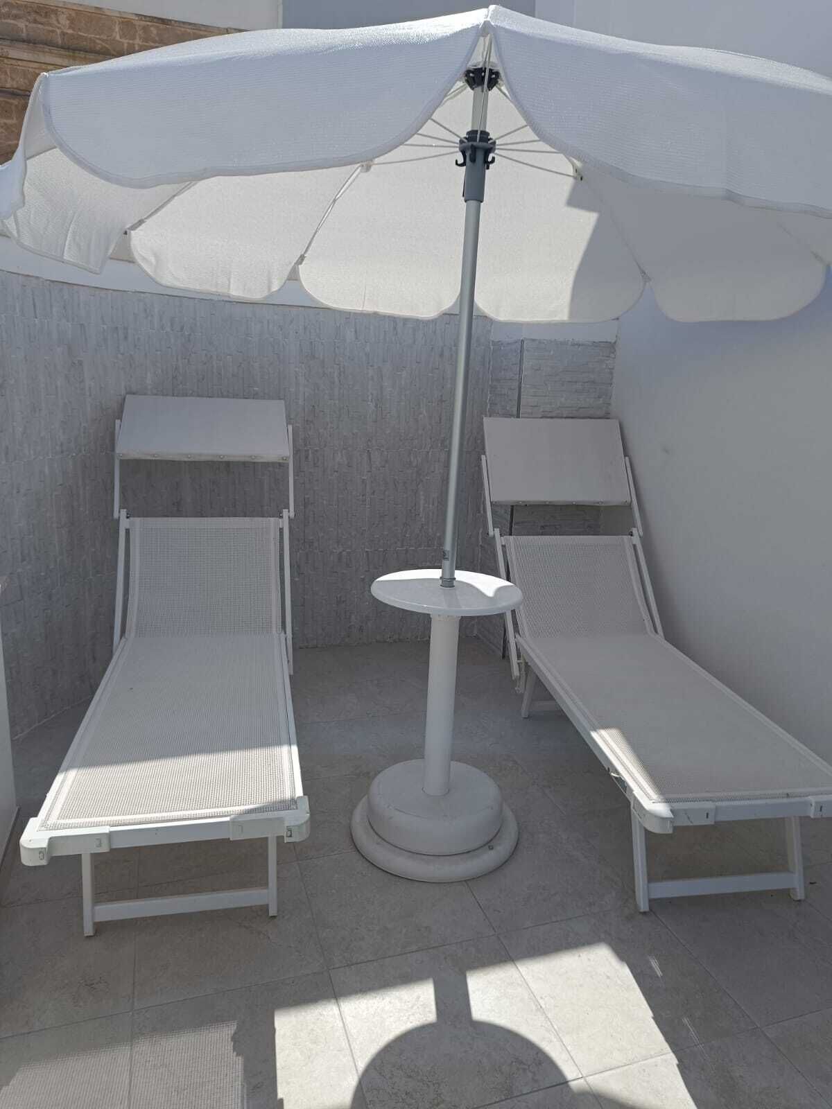 Un área de estar al aire libre con luz solar, con sillones blancos y una mesa central, todo ello rodeado por un dosel blanco.