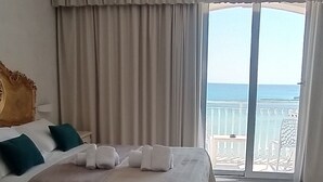 Een hotelkamer met een groot bed, een balkon met uitzicht op zee en een marmeren vloer.
