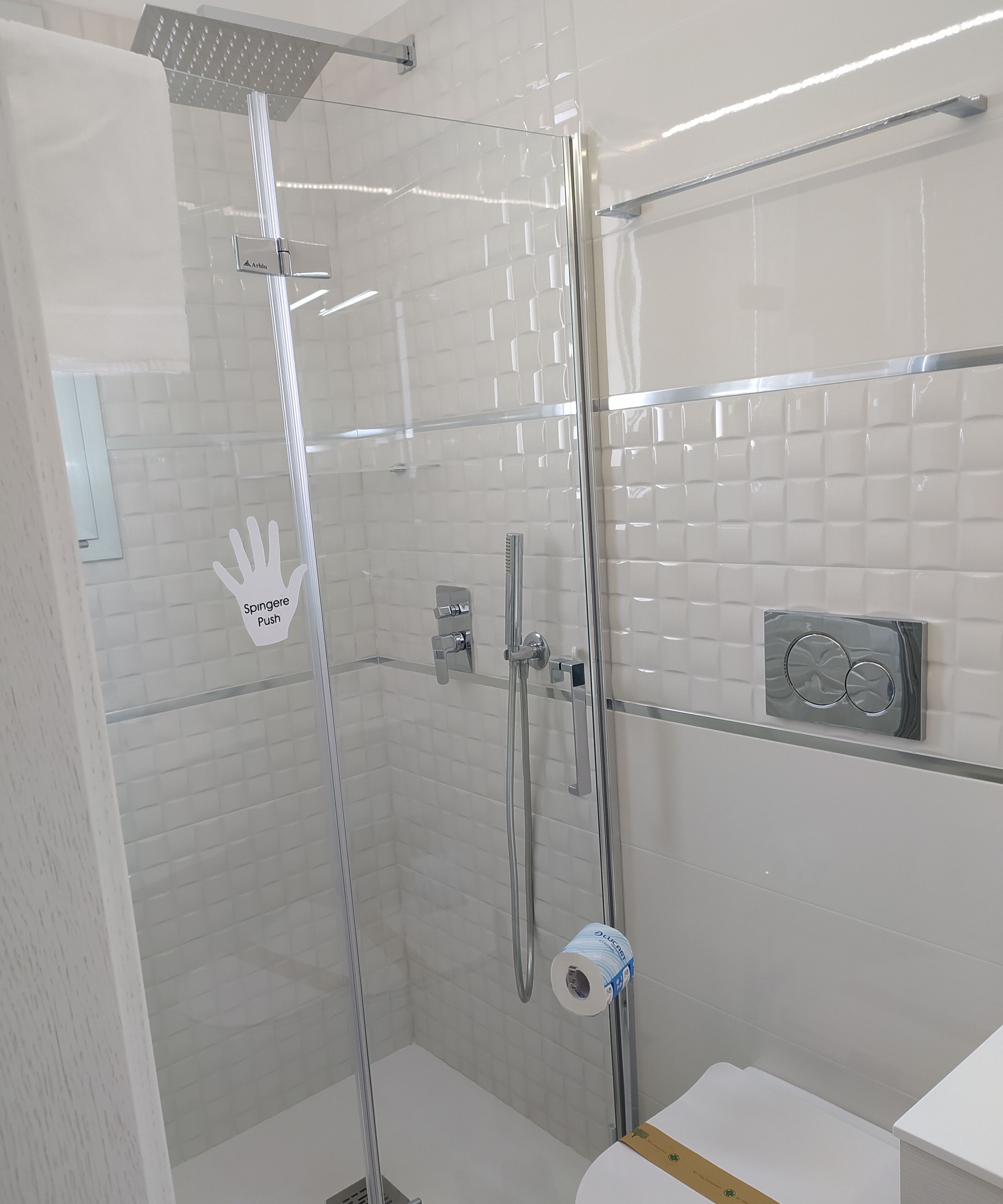 A modern bathroom with a glass-enclosed shower, chrome fixtures, and a toilet paper holder.