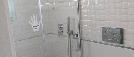A modern bathroom with a glass-enclosed shower, chrome fixtures, and a toilet paper holder.