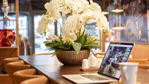A dining area with a laptop, a white mug, and a floral centerpiece on a wooden table. - ROX Hotel Ankara (Ankara)