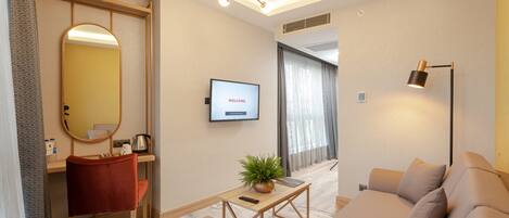 Una habitación de hotel moderna con un sofá, una mesita con una planta, un televisor mostrando 'WELCOME' y un espejo.