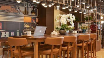 Un restaurante moderno con mesas y sillas de madera, lámparas colgantes y un ordenador portátil sobre una mesa.