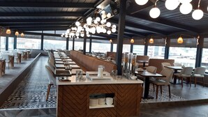 A modern restaurant with a long counter, white chairs, and a view of the city through large windows. - ROX Hotel Ankara (Ankara)