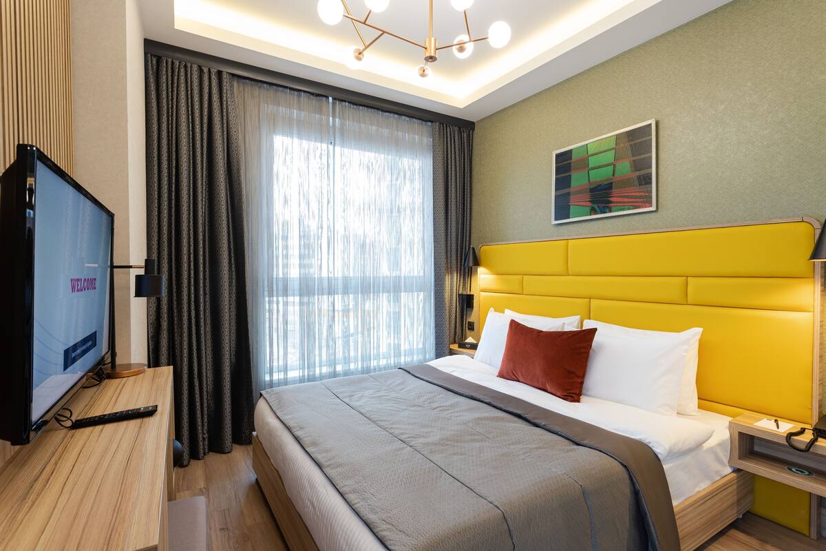 Una habitación de hotel moderna con cama, televisor, escritorio y ventana con cortinas.