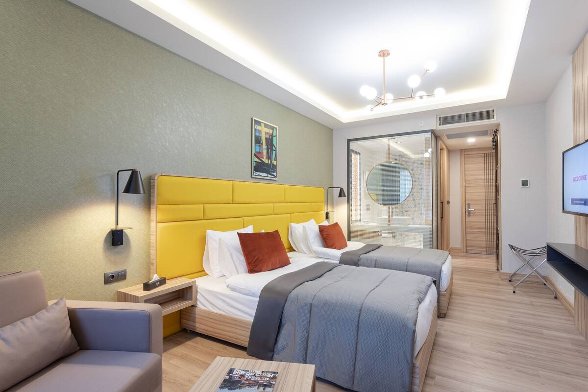Una habitación de hotel moderna con dos camas, un sofá, un televisor y un amplio ventanal.