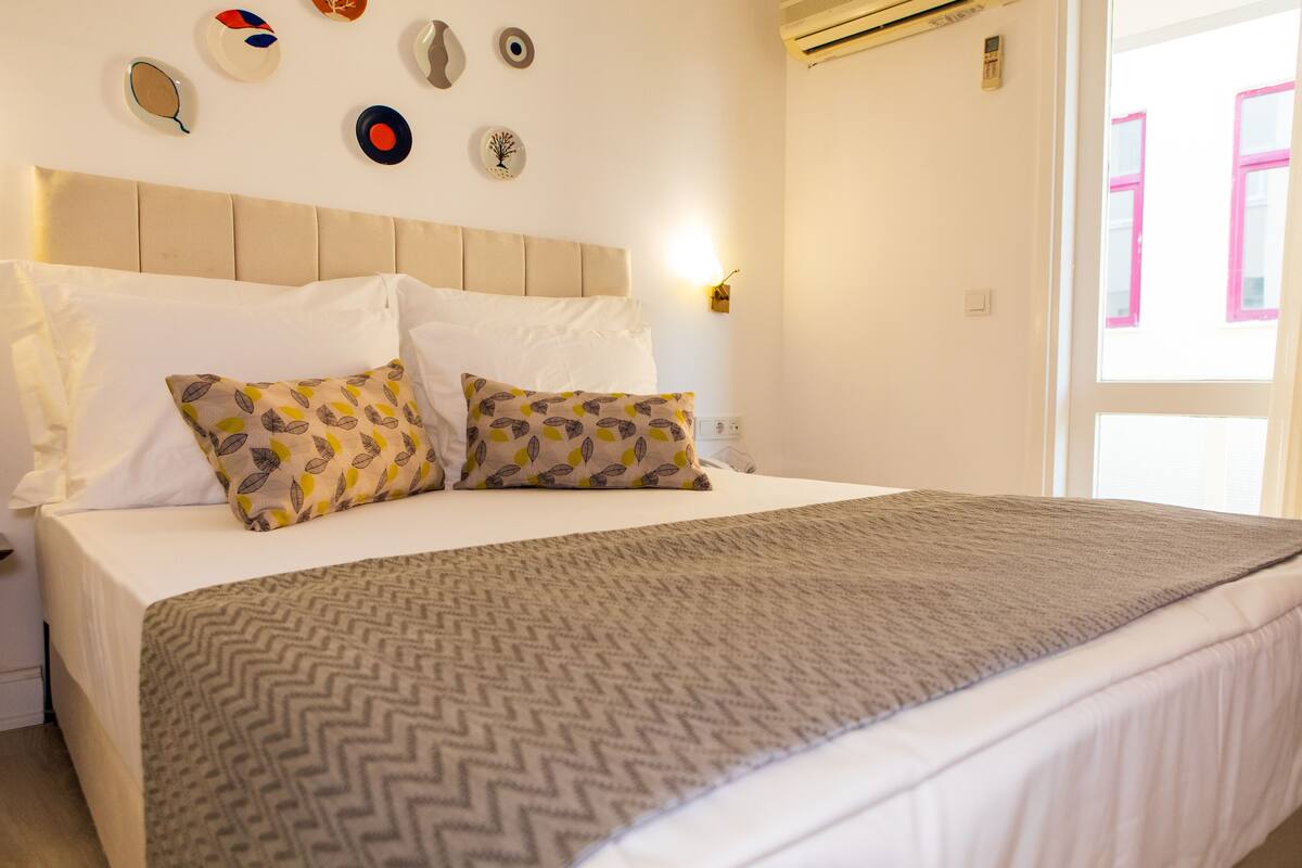 Una cama impecablemente arreglada con almohadas estampadas, un edredón de diseño geométrico en forma de chevrón y decoración de pared que incluye platos y un diseño de árbol.