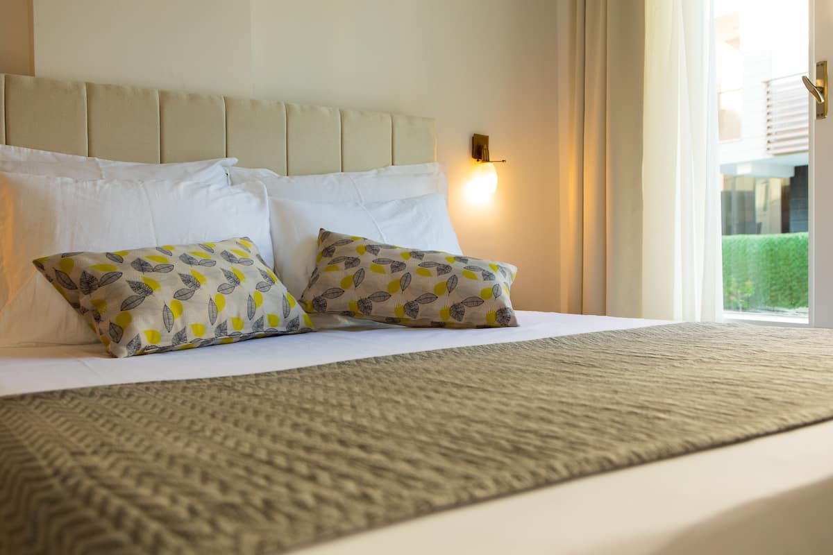 Una cama bien hecha con un cojín estampado, un cabecero y una lámpara fijada a la pared.