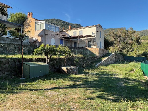 A two-story house with a stone wall, a small tree, and a green fence.