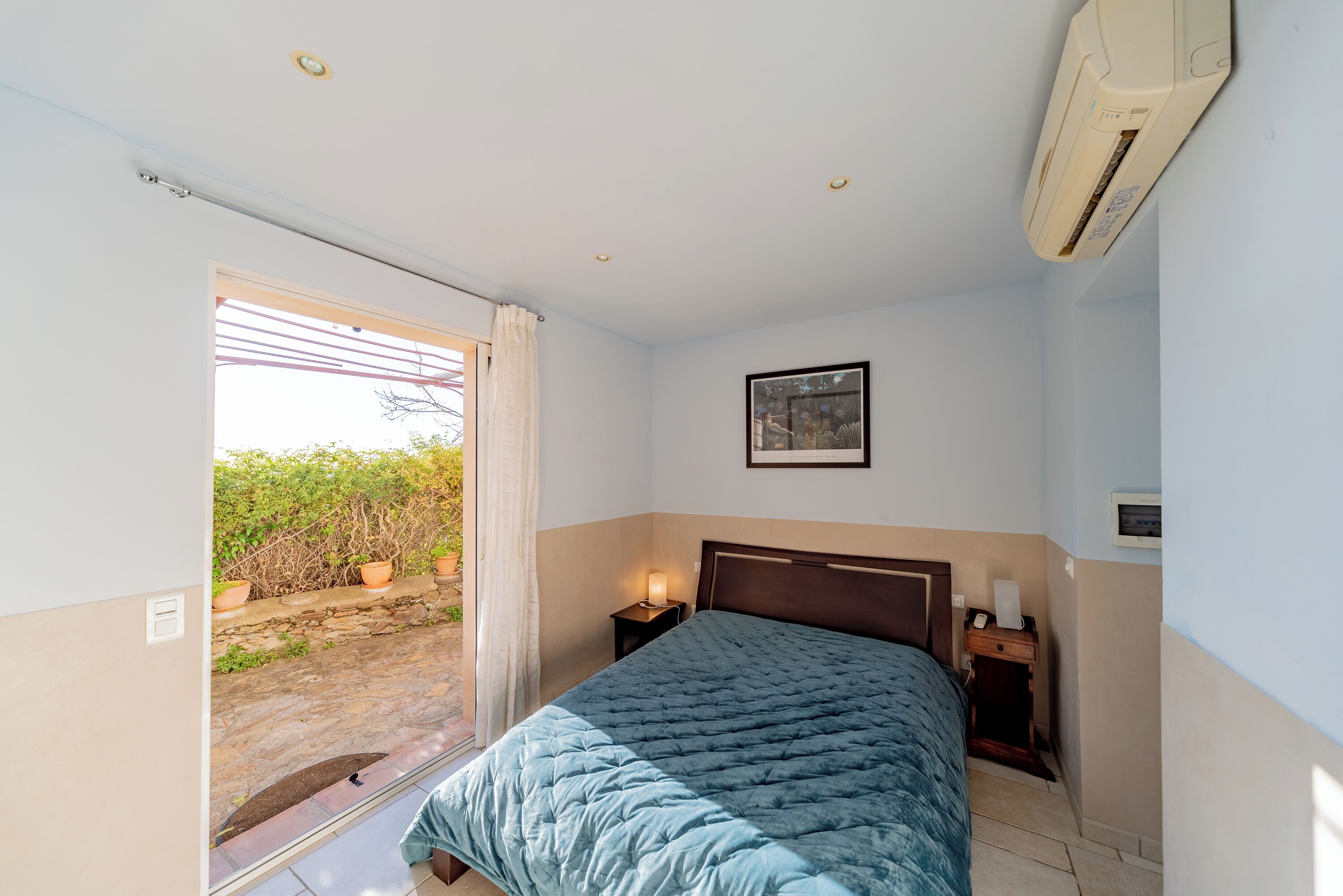 Een slaapkamer met een bed, nachtkastje, airconditioning en een wanddecoratie, met uitzicht op het exterieur.
