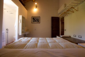 Une chambre à coucher comprenant un lit, une table de chevet, un miroir, un luminaire suspendu, un tableau encadré accroché au mur et une porte en bois.