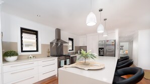 A modern kitchen with white cabinetry, stainless steel appliances, and a central island with bar stools. - Pets Allowed Burleigh Beach Pad (Burleigh Waters)