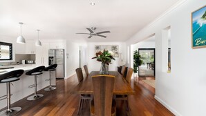 A modern kitchen with white cabinets, a stainless steel refrigerator, and a bar area with black stools. - Pets Allowed Burleigh Beach Pad (Burleigh Waters)