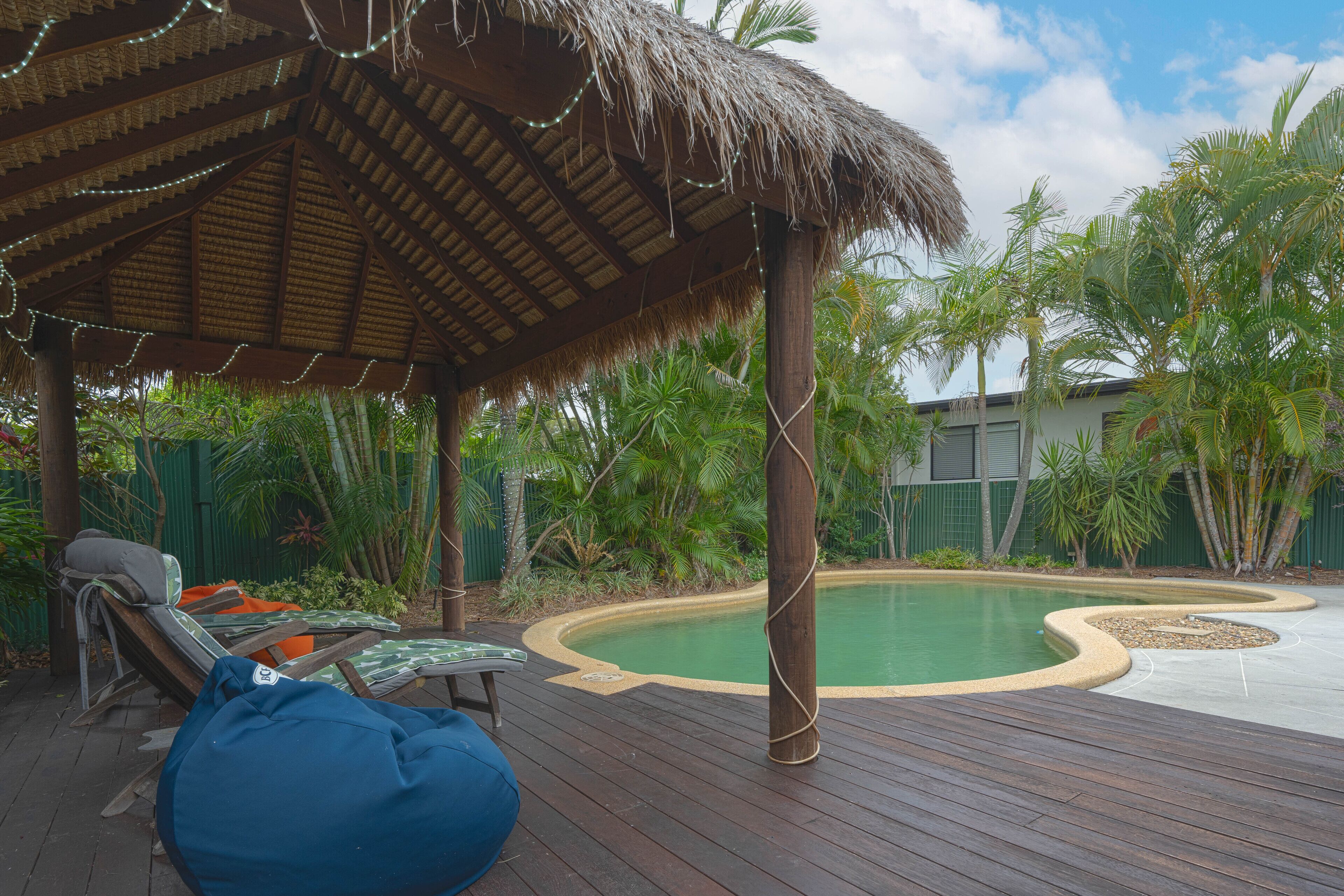 Terraza de madera con sillones, una estructura de techo de paja y una piscina.