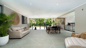 A spacious living area with a sofa, a dining table, and chairs, surrounded by potted plants. - Pets Allowed Burleigh Beach Pad (Burleigh Waters)