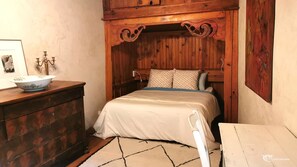 A bedroom with a wooden headboard, a bed with a white bedspread, a dresser with a bowl on top, and a small table. - Large cottage in renovated Templar mas - panoramic view (Occitanie)