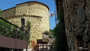 A stone building with a round tower, outdoor seating, and a metal railing. - Large cottage in renovated Templar mas - panoramic view (Occitanie)