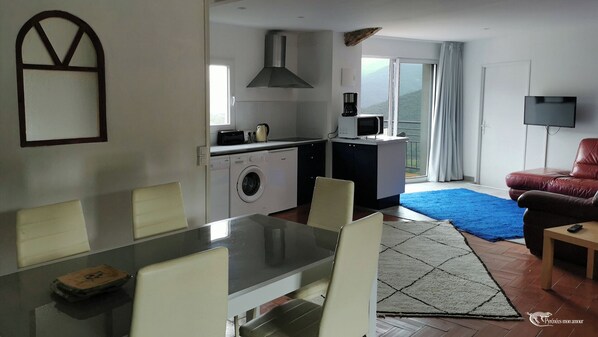 A compact living space with a dining area, a kitchenette, a washing machine, a TV, and a sofa. - Large cottage in renovated Templar mas - panoramic view (Occitanie)