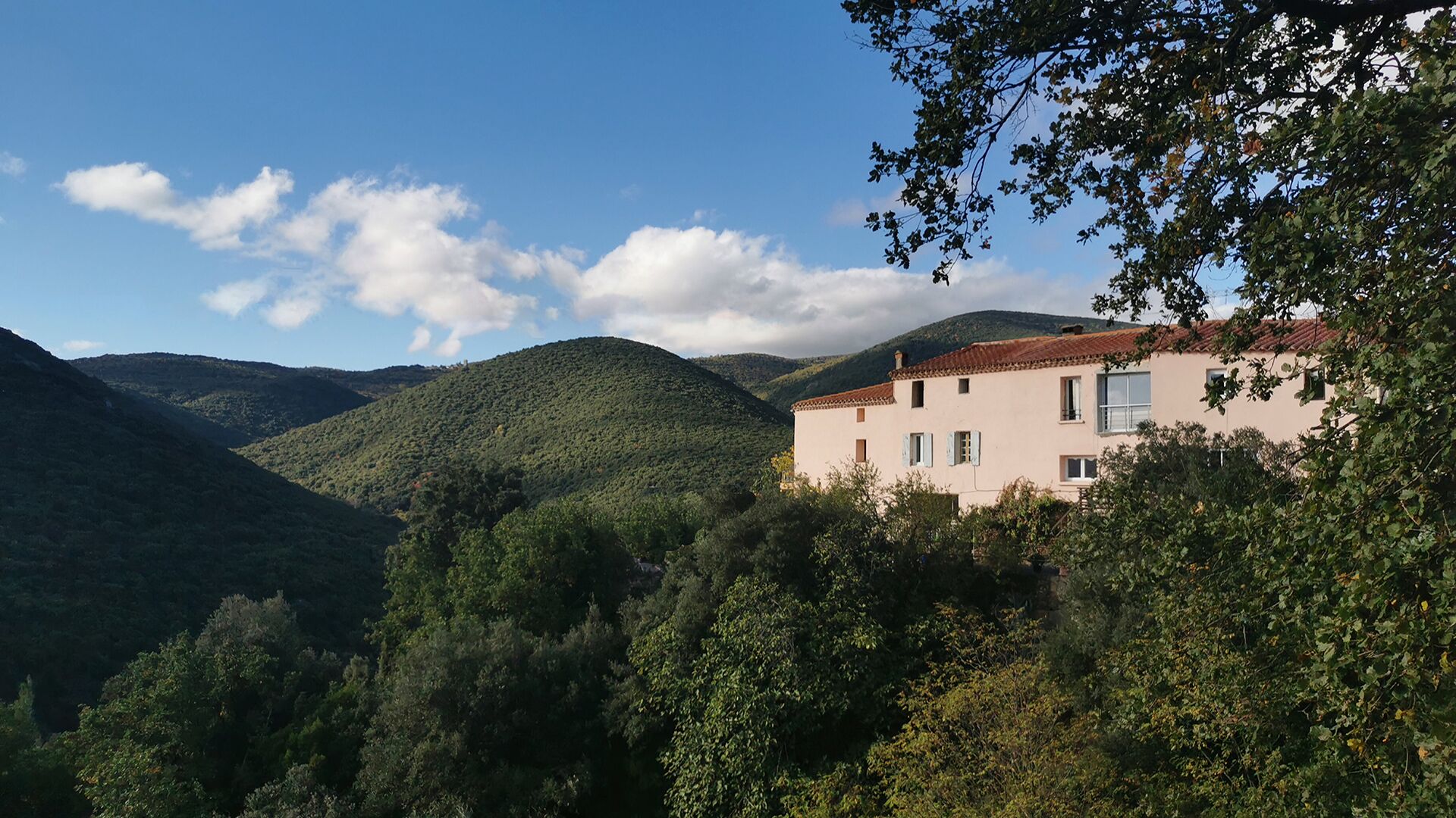 A building with a red-tiled roof, surrounded by lush greenery and hills.