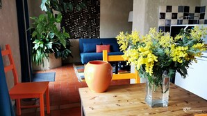 A cozy living area with a sofa, a wooden table with a vase of yellow flowers, a potted plant, and a red chair. - Small nest for 2 with 180 ° view on wooded hills in a cozy cottage (Occitanie,)