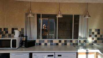 Cocina con microondas, cafetera y lavavajillas. Hay luces colgantes y una ventana con vistas.