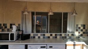 A kitchen with a microwave, coffee maker, and dishwashers. There are three pendant lights and a window with a view.