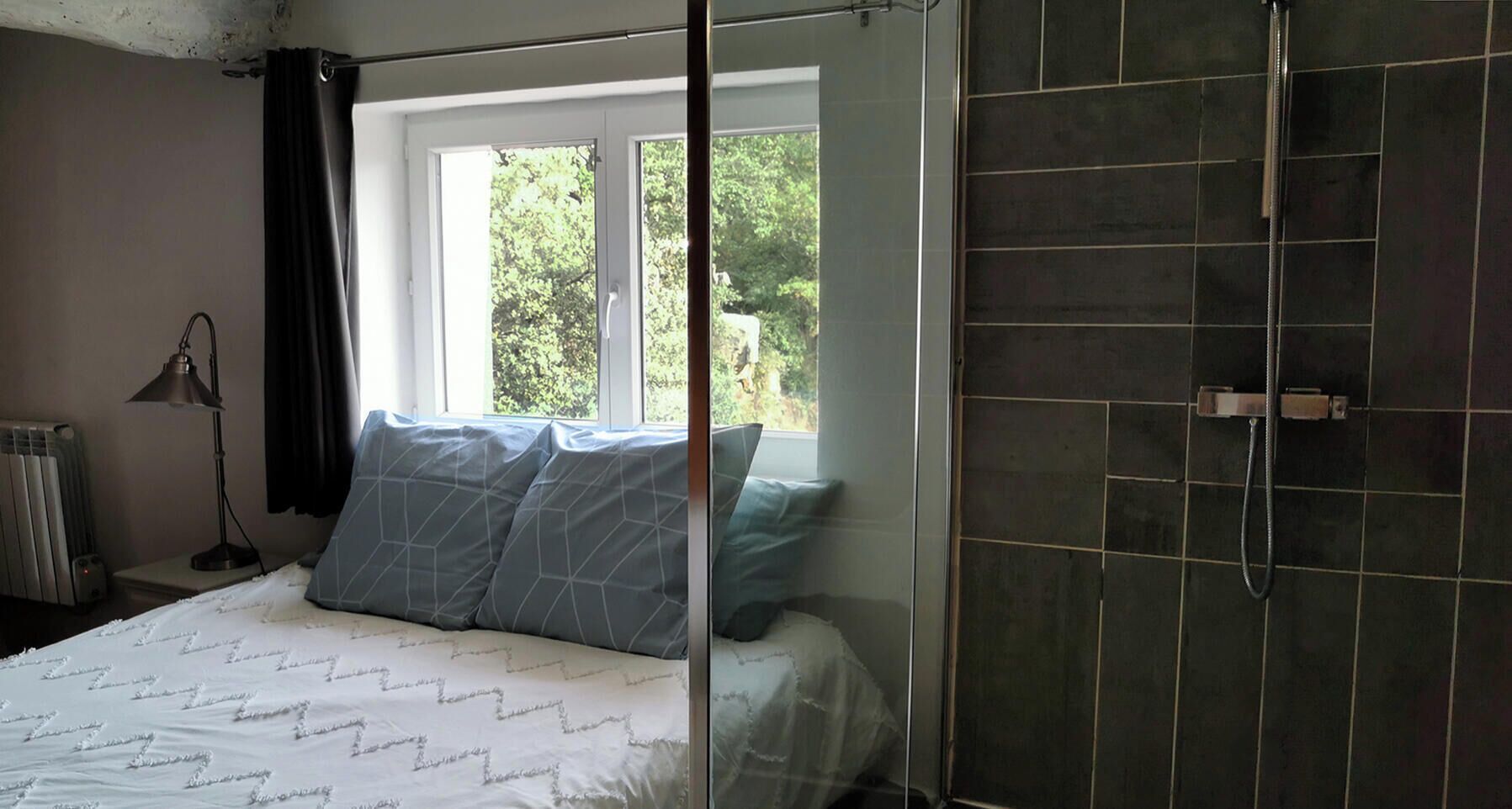 A bedroom with a bed, a window, a radiator, and a shower area.