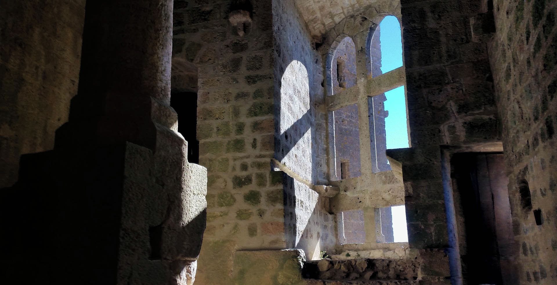 Vista interior de un edificio de piedra con ventanas arqueadas y una columna central.