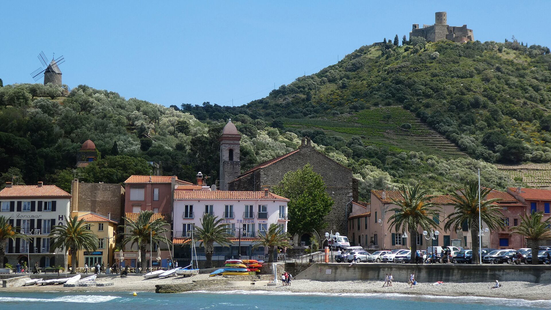 A coastal town with a historic windmill, a church, and a castle on a hill.