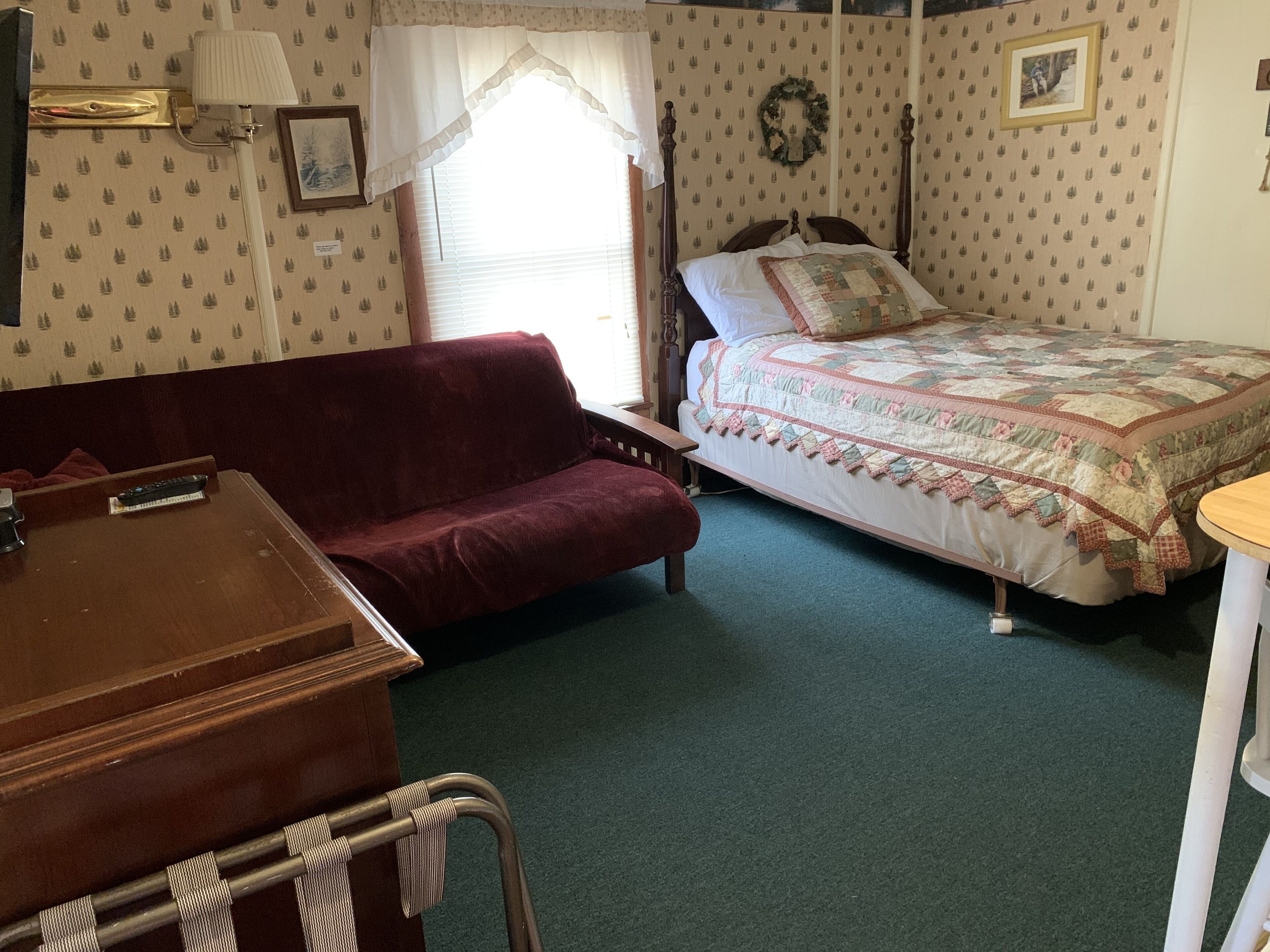 A room with a wooden bed, a red sofa, a wooden table, and a wheelchair.