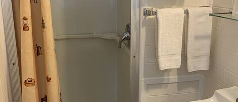 A bathroom with a glass shower enclosure, a white sink, and two white towels on a rack.