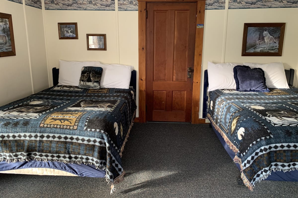A room with two beds, a wooden door, and wall art depicting wolves.