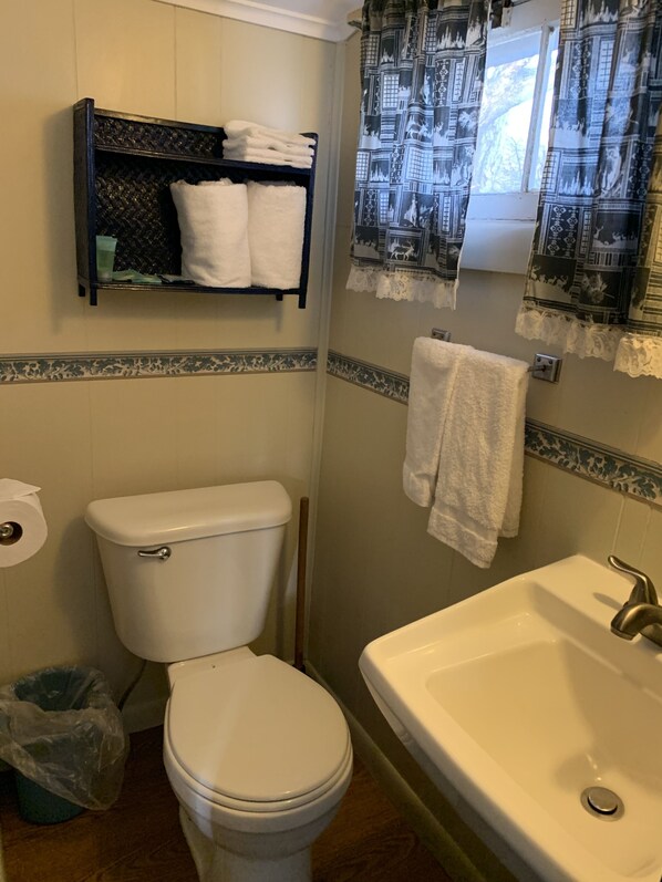A bathroom with a toilet, a sink, a shelf with towels, and patterned curtains.