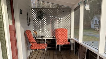 A covered porch with wooden flooring, two red patterned chairs, a small table, and a green mat.