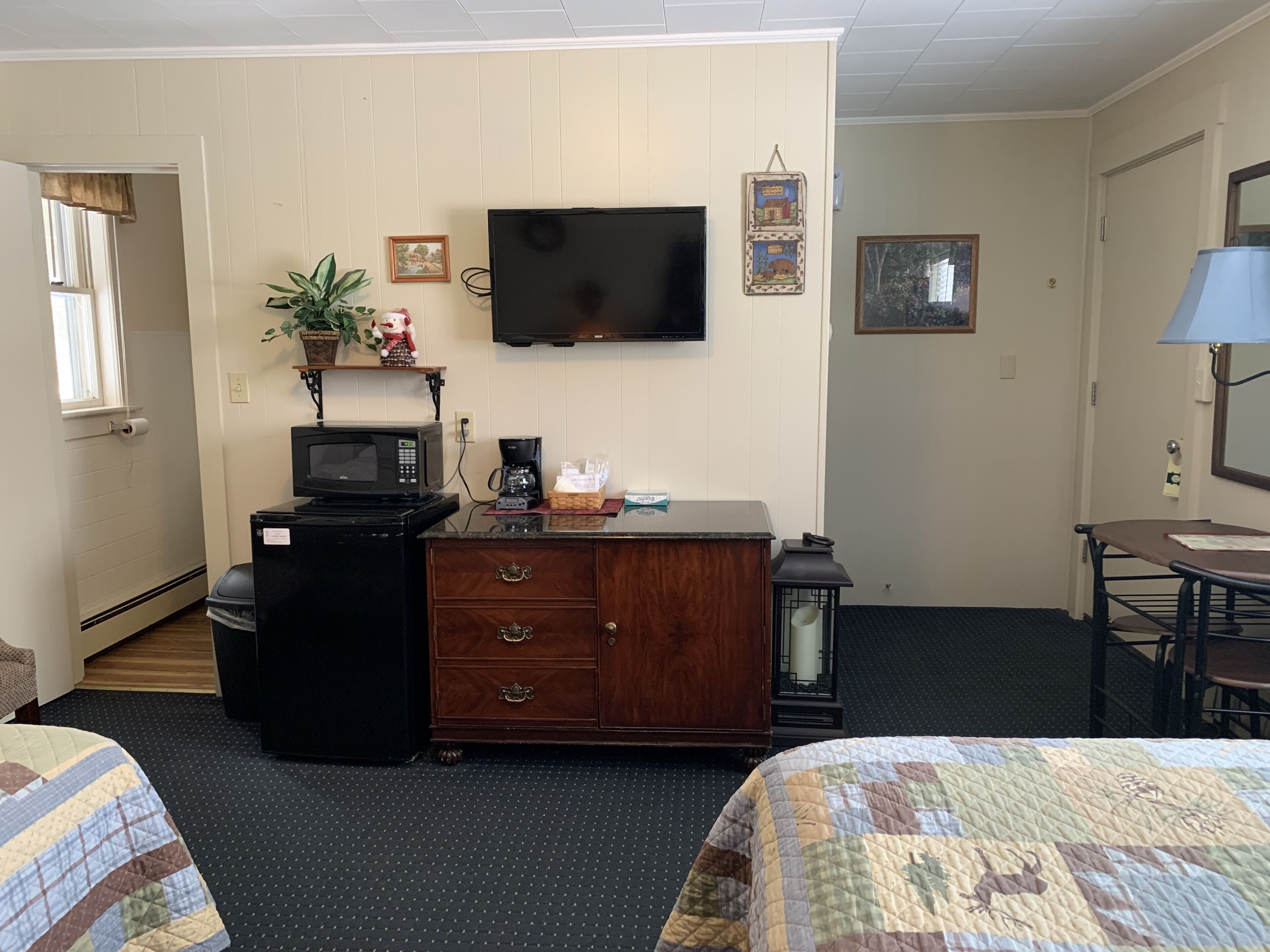 A hotel room with a wooden dresser, a microwave, a coffee maker, a television, and a bed with a quilt.