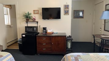 A hotel room with a wooden dresser, a microwave, a coffee maker, a television, and a bed with a quilt.