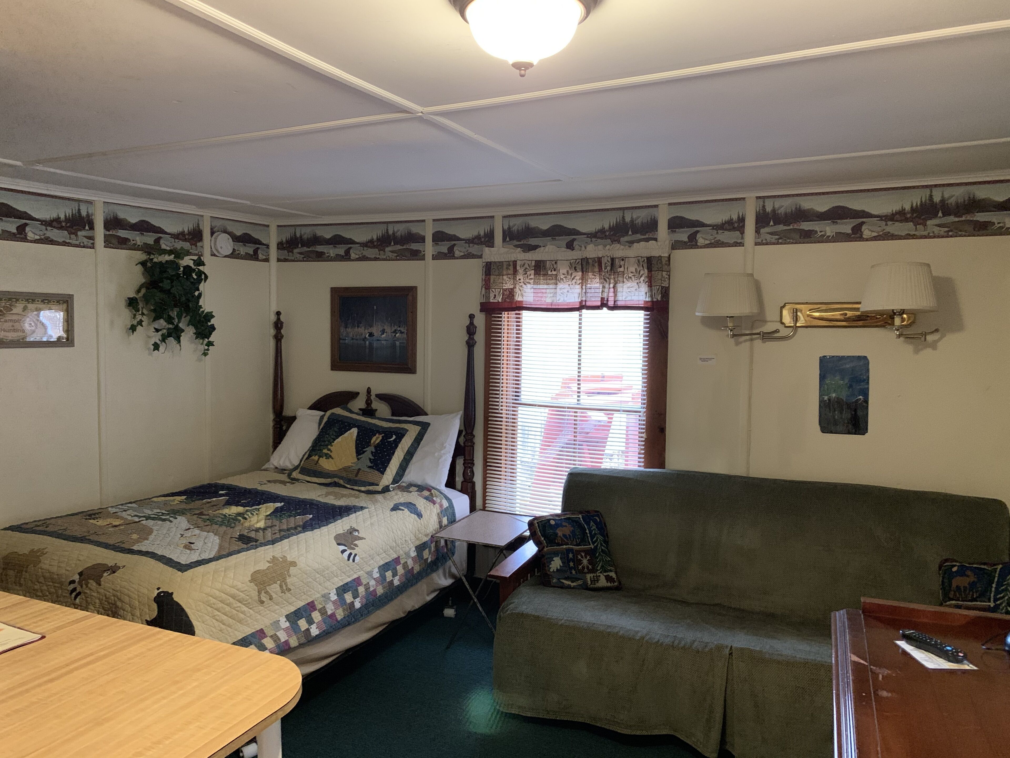 A bedroom with a bed, a green sofa, a window with blinds, and wall decorations.