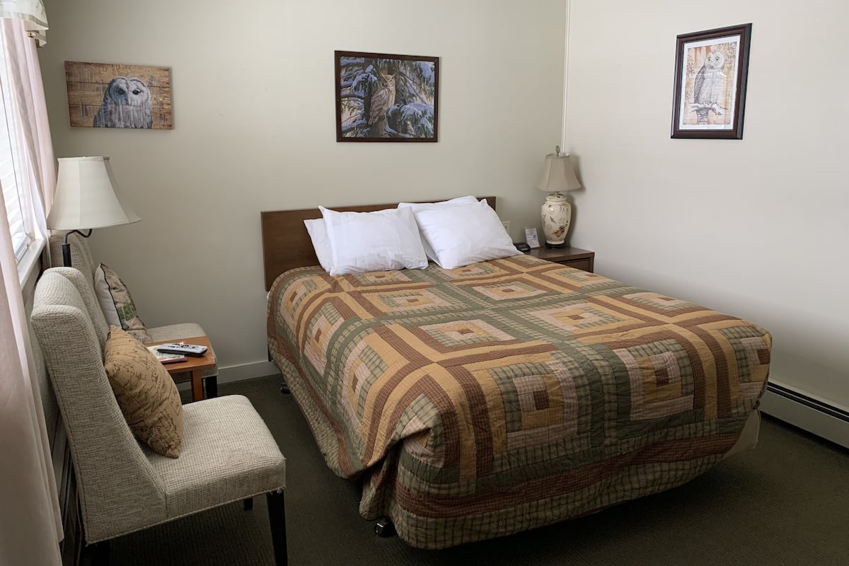 A hotel room with a bed, a chair, a nightstand, and two wall-mounted lamps.