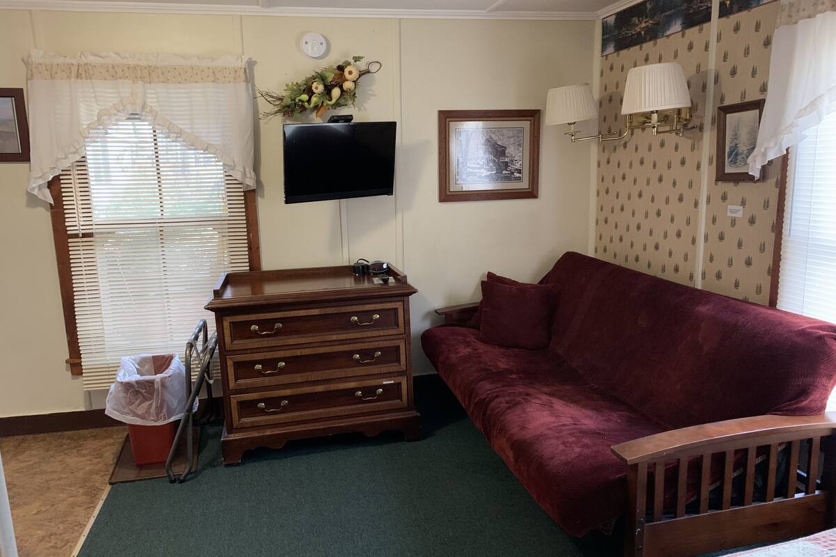 A room with a wooden dresser, a red sofa, a television mounted on the wall, and a window with blinds.