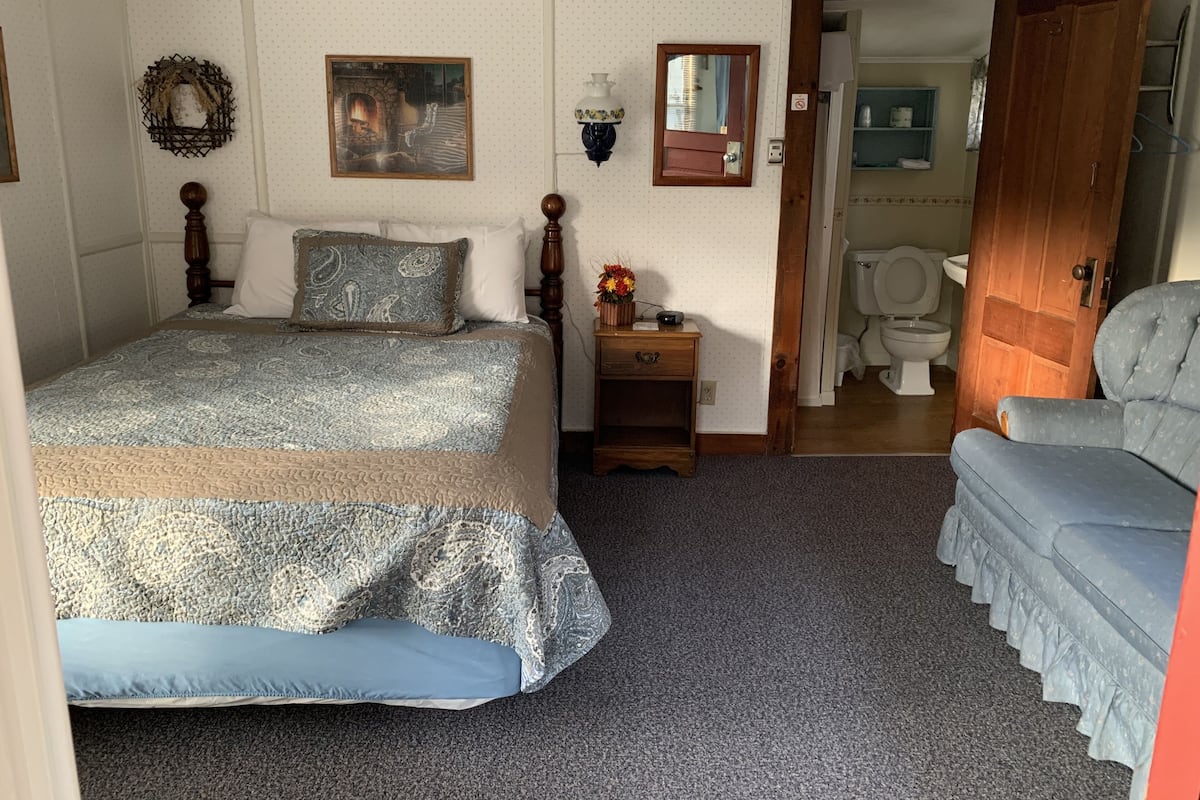 A bedroom with a bed, bedside table, dresser, and a door leading to a bathroom.