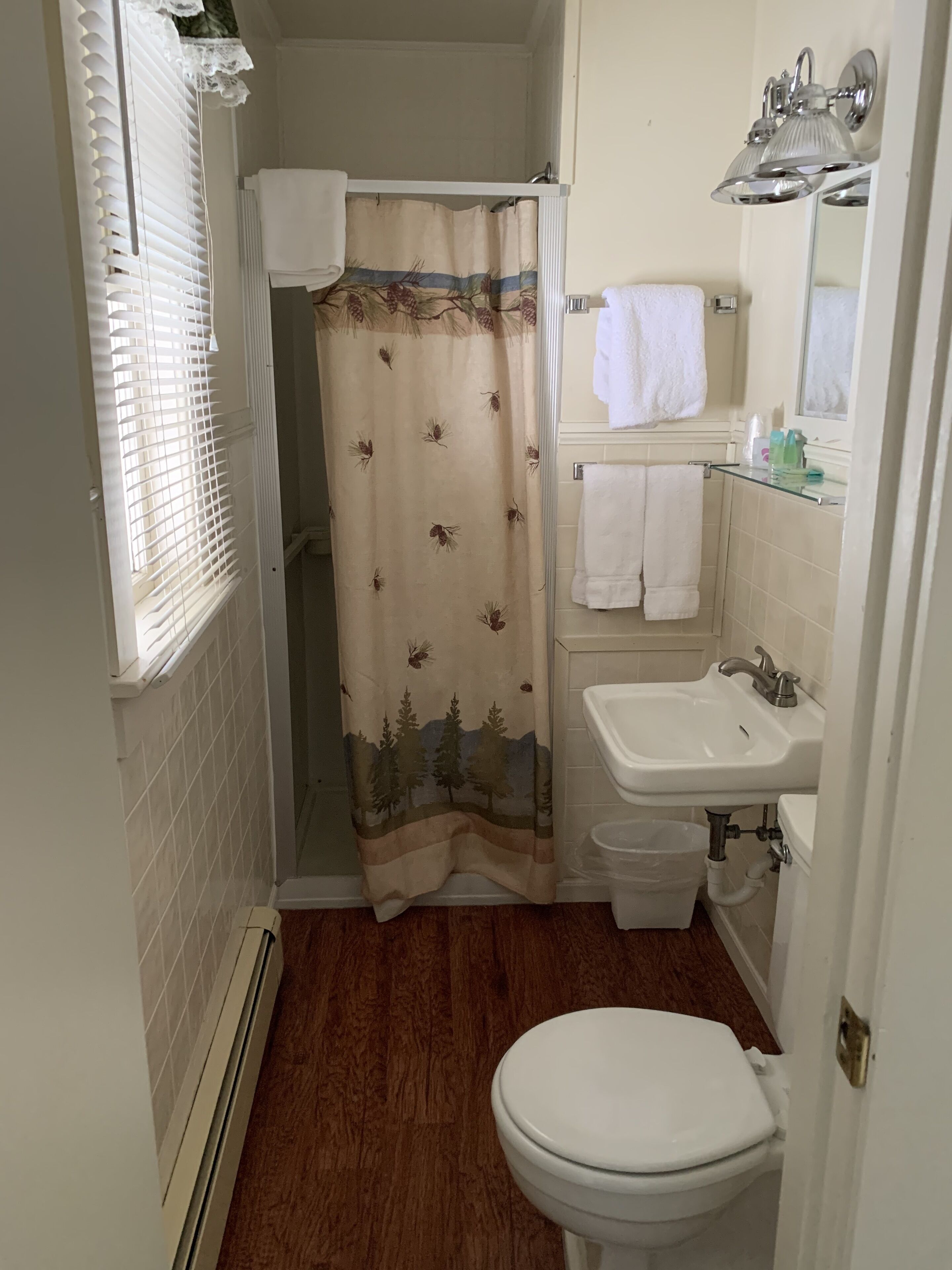 A bathroom with a shower curtain, a sink, a toilet, and a window with blinds.