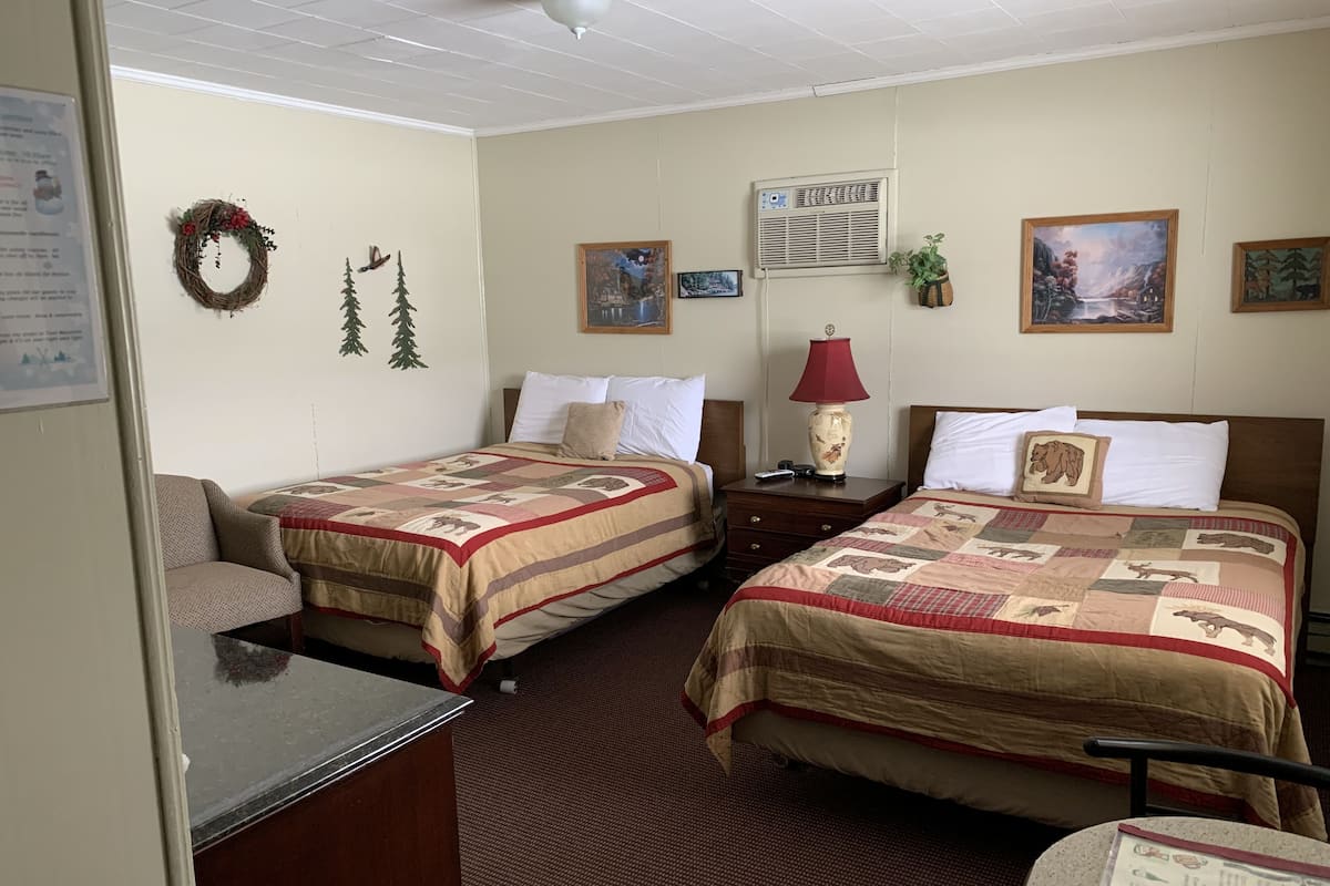 A hotel room with two beds, a desk, a chair, a lamp, and a small table.