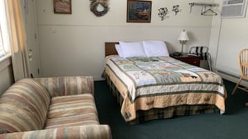 A bedroom with a bed, a chair, a nightstand, and a wall with a wreath and two framed pictures.