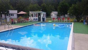 Ein Schwimmbecken mit Rettungsschwimmerstation, Liegestühlen und einem kleinen Gebäude mit rotem Dach.