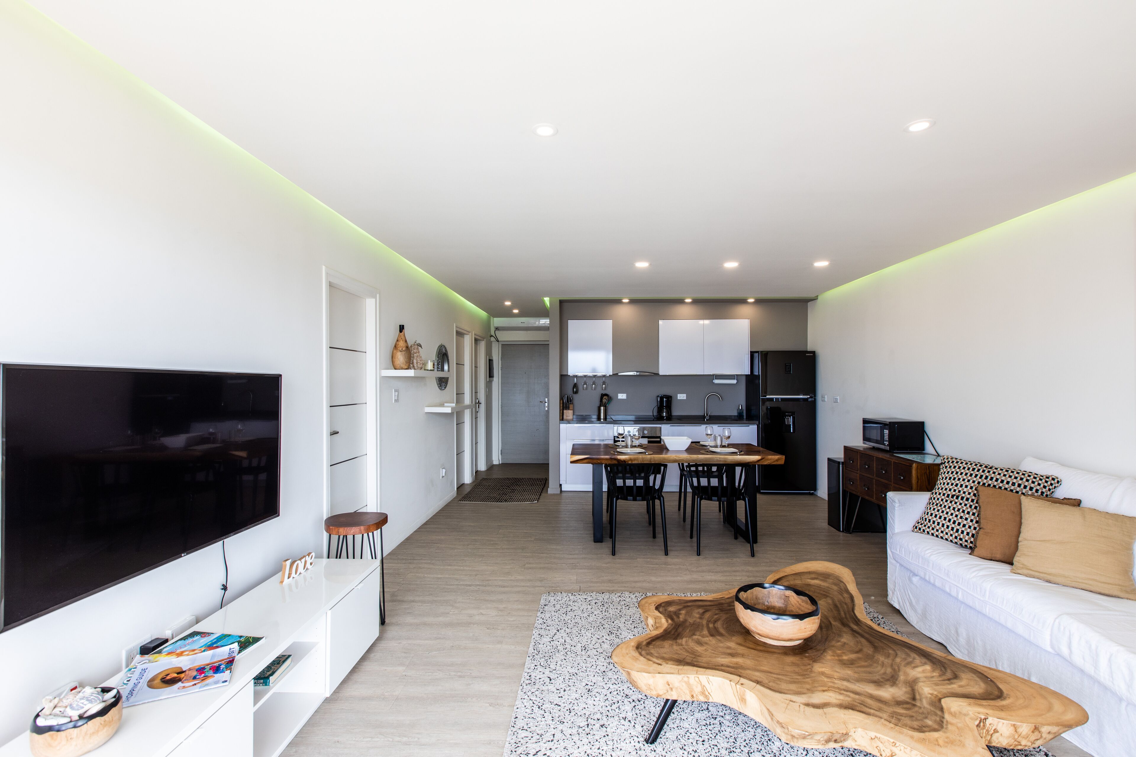 A modern living room with a flat-screen TV, a wooden coffee table, and a white sofa.