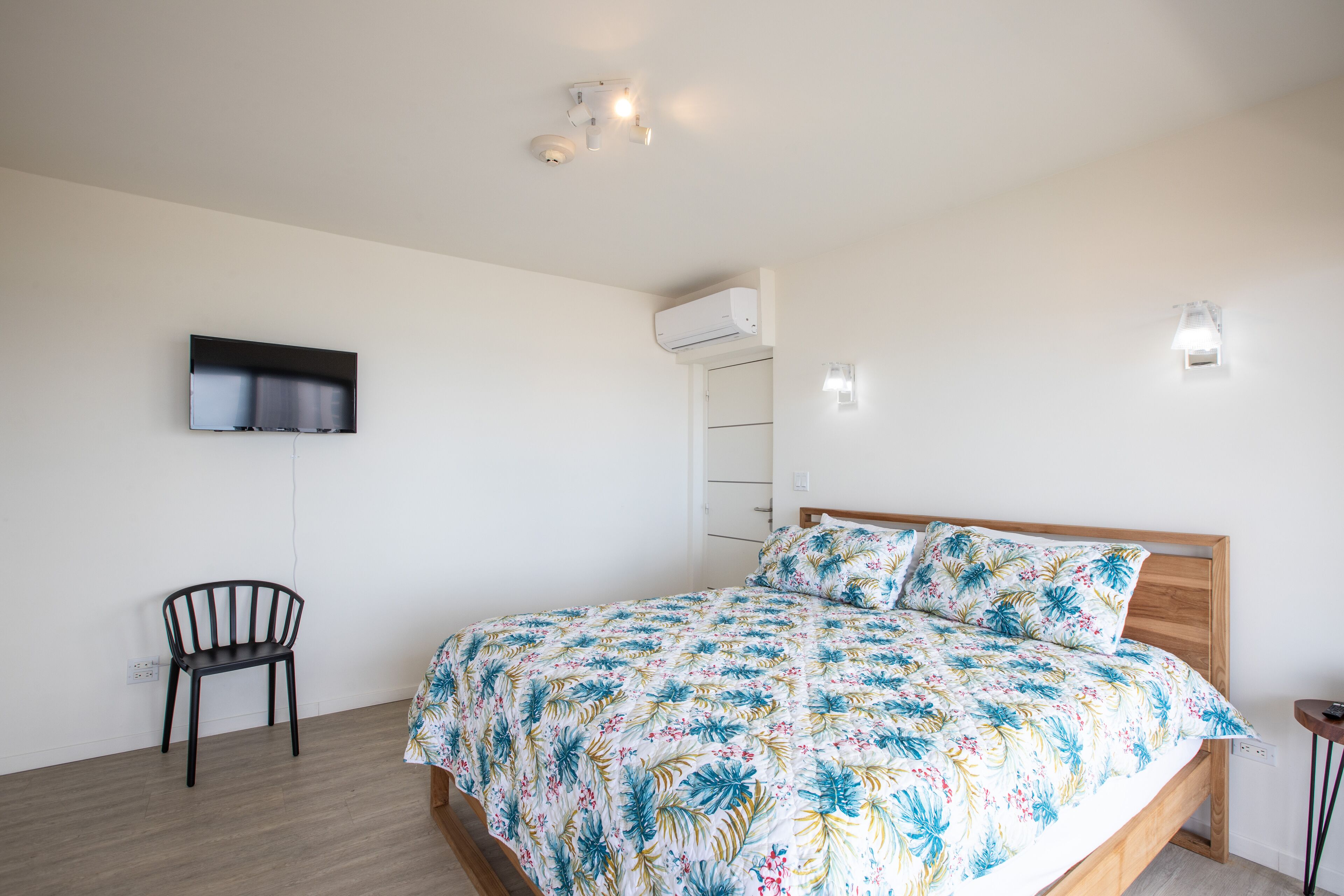Een slaapkamer met een bed, een stoel, een aan de muur bevestigde televisie en een airconditioner.