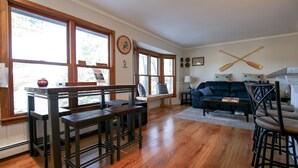 Ein geräumiges Wohnzimmer mit Holzboden, einem blauen Sofa, einem Couchtisch und einem Essbereich mit Holzsesseln und einer Bank.