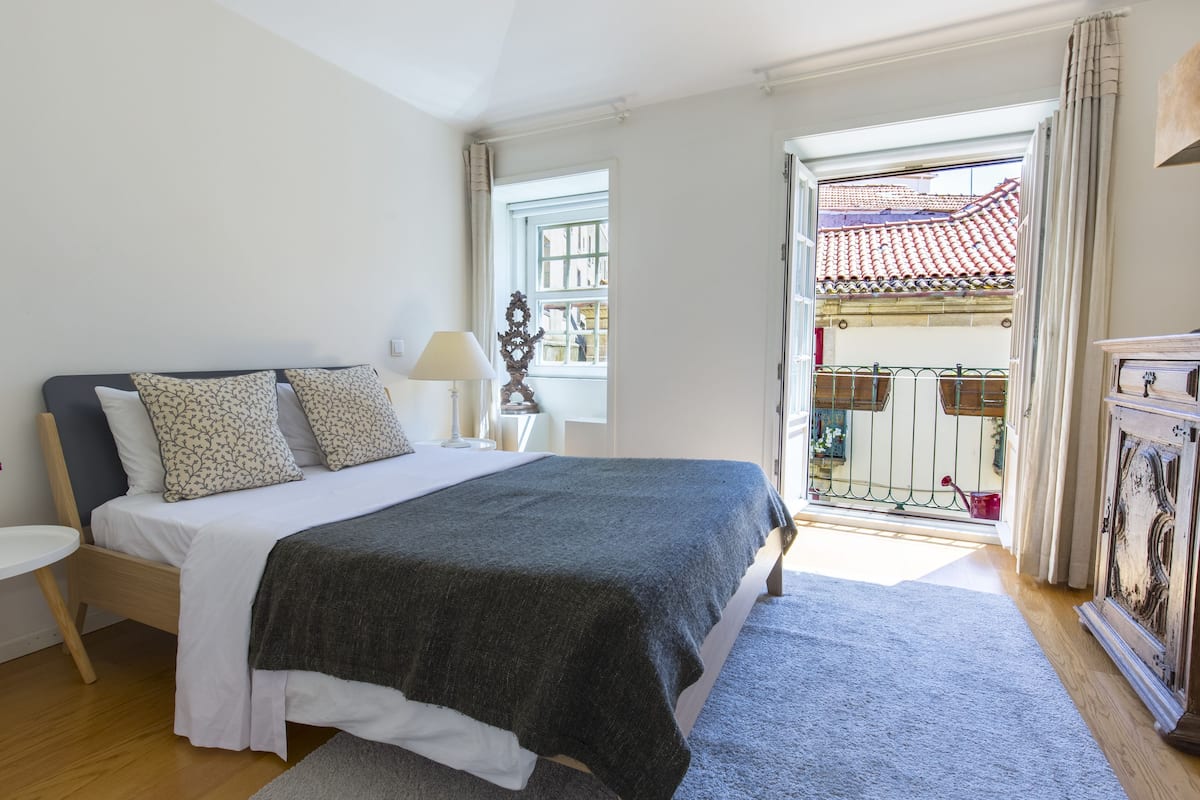 A bedroom with a bed, bedside table, lamp, and a view of the outside balcony.
