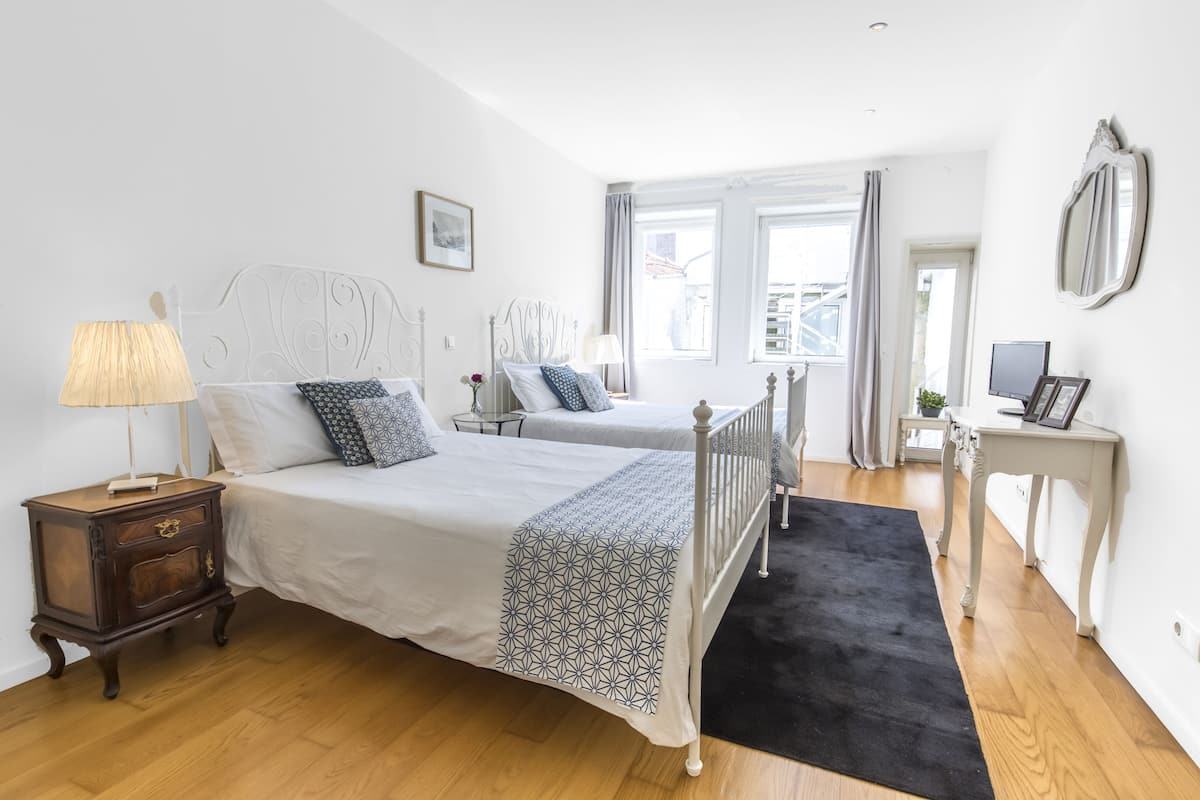 A bedroom with two beds, a bedside table with a lamp, a small table with a plant, and a mirror on the wall.